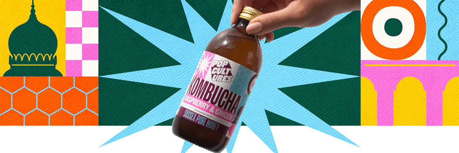 Bottle of Kombucha held by a hand against a colorful geometric background